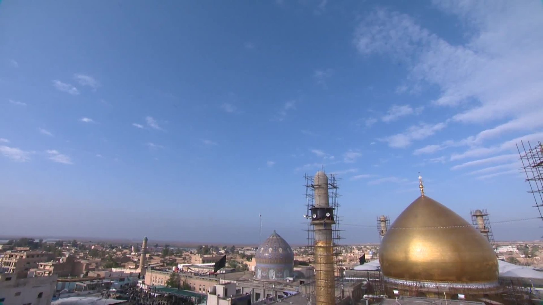 The golden dome of the al-Askari shrine in Samarra beside the blue dome over the Sardab, with a minaret under scaffolding