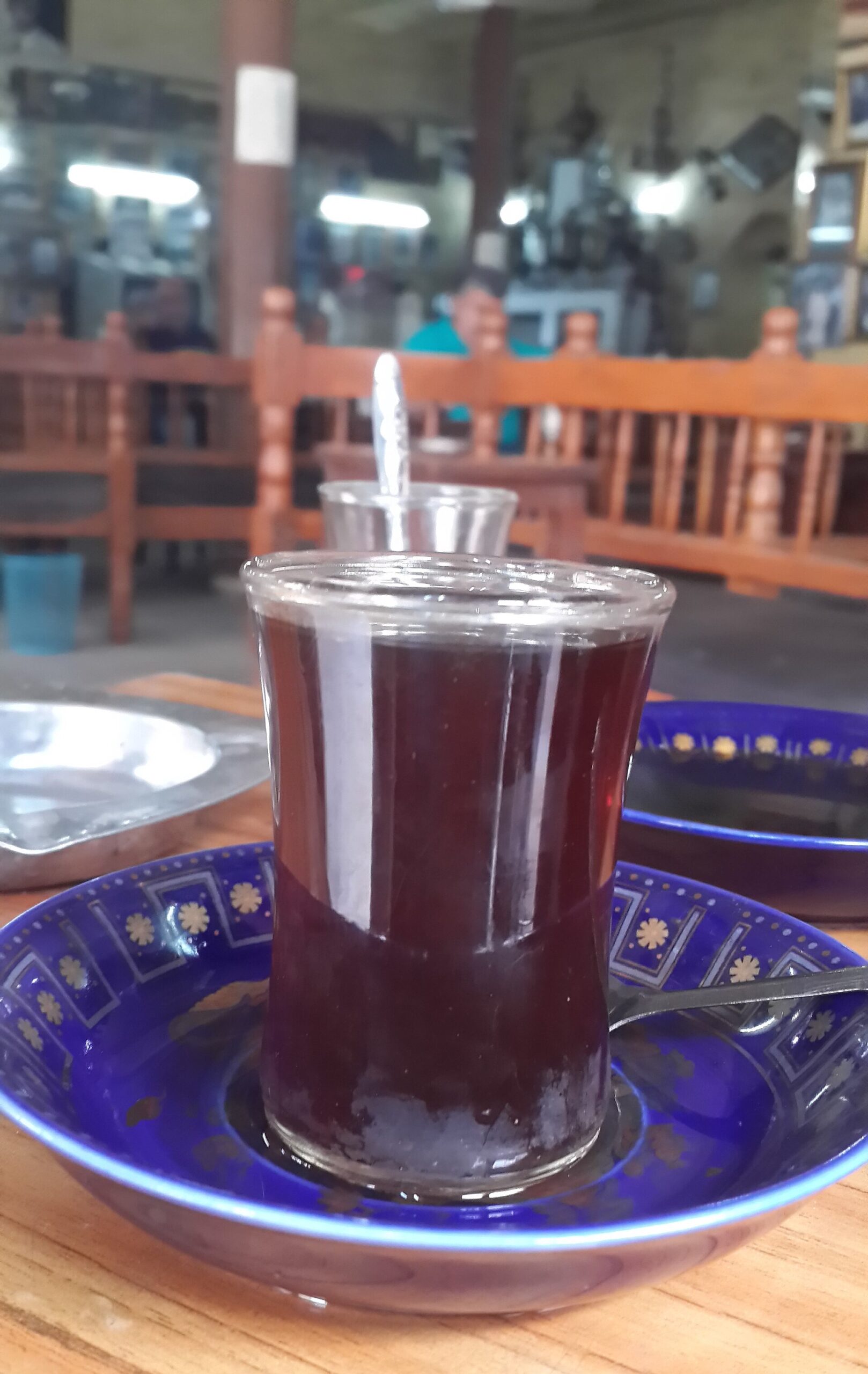 Glass istikan of black tea on a blue enamel saucer on a wooden table inside a Baghdad heritage cafe