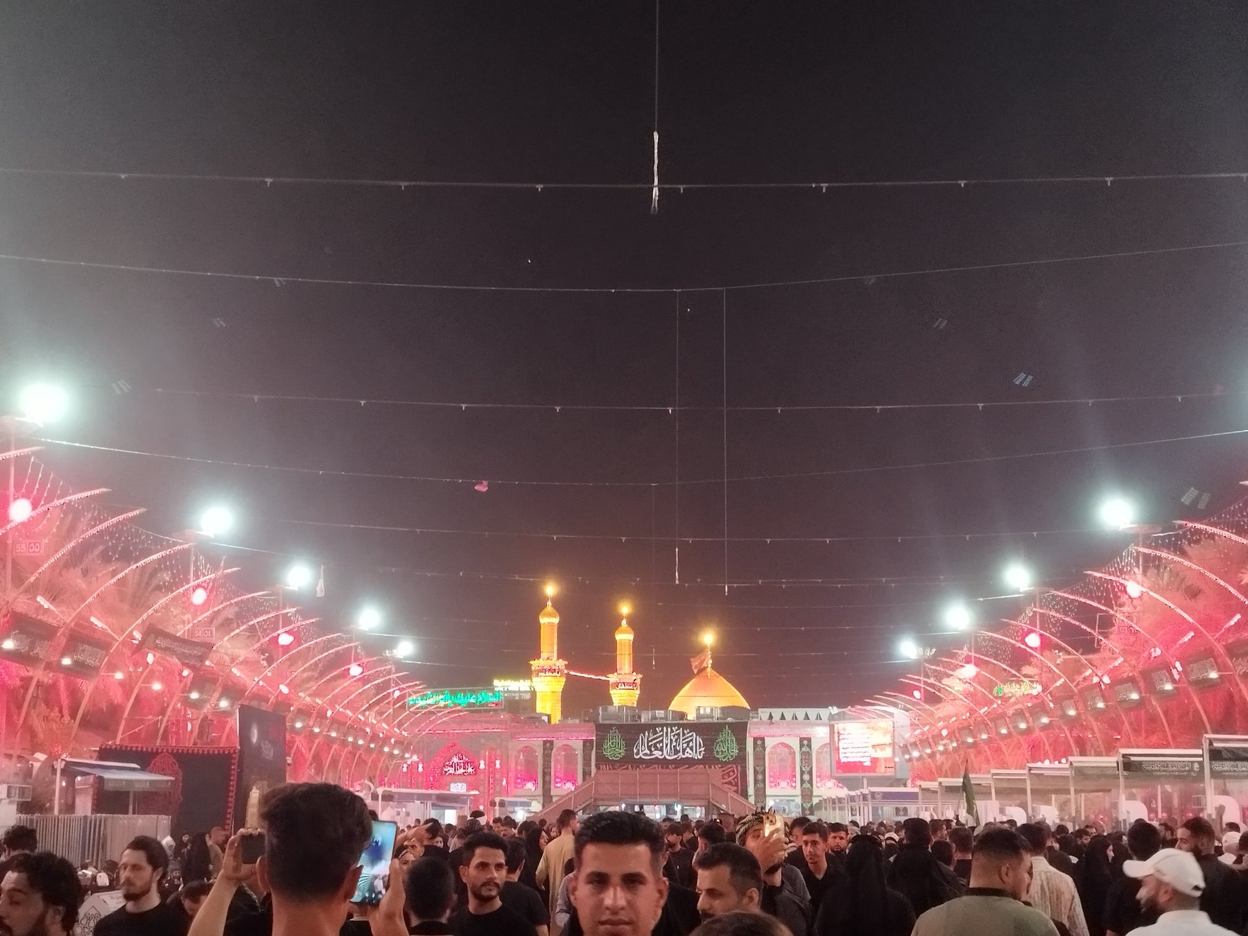 Pilgrims filling the lit Bayn al-Haramayn corridor between the Imam Hussein and al-Abbas shrines in Karbala at night