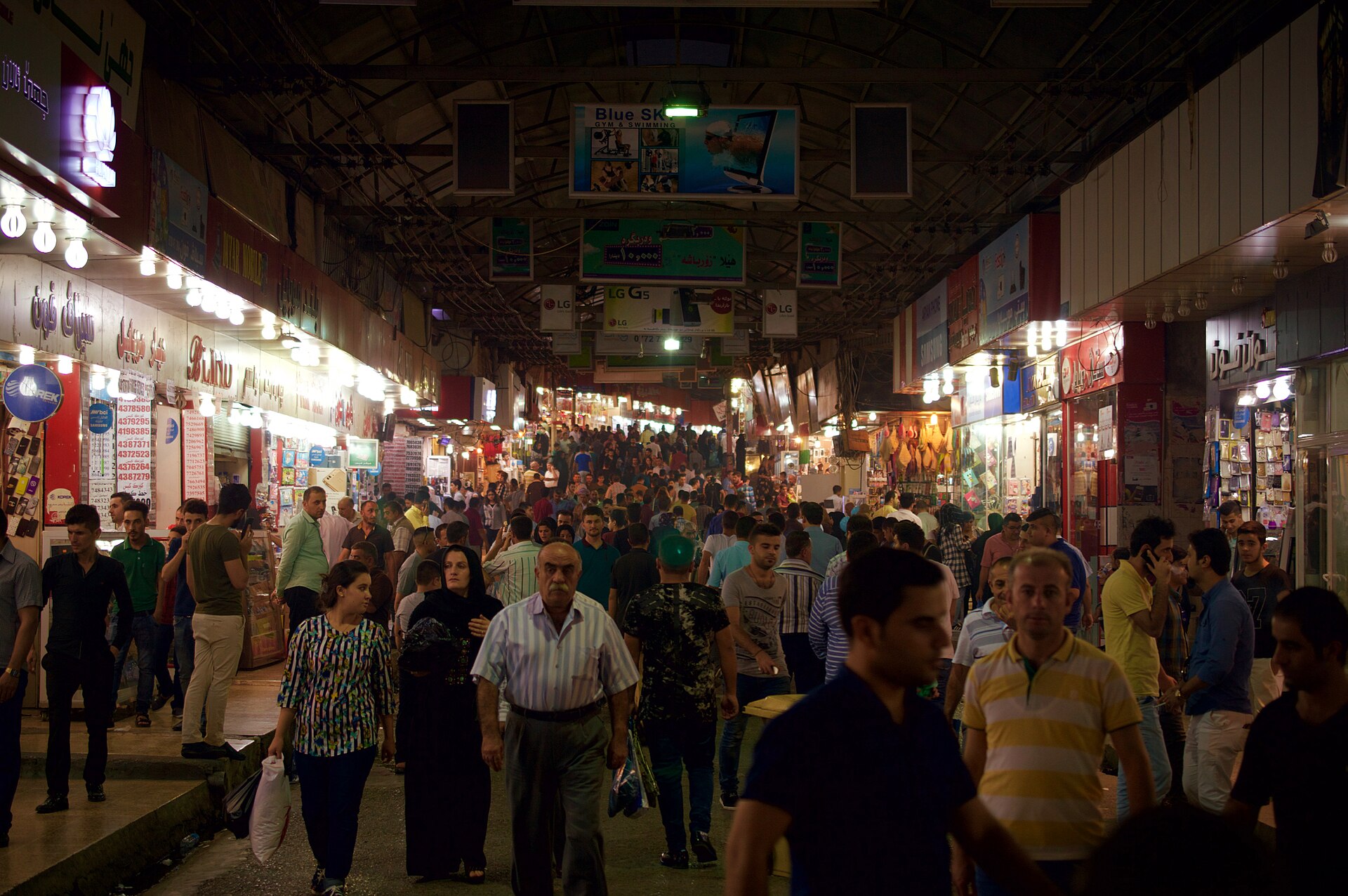 Shoppers filling a covered arcade of the Duhok bazaar, lined with electronics and clothing shops