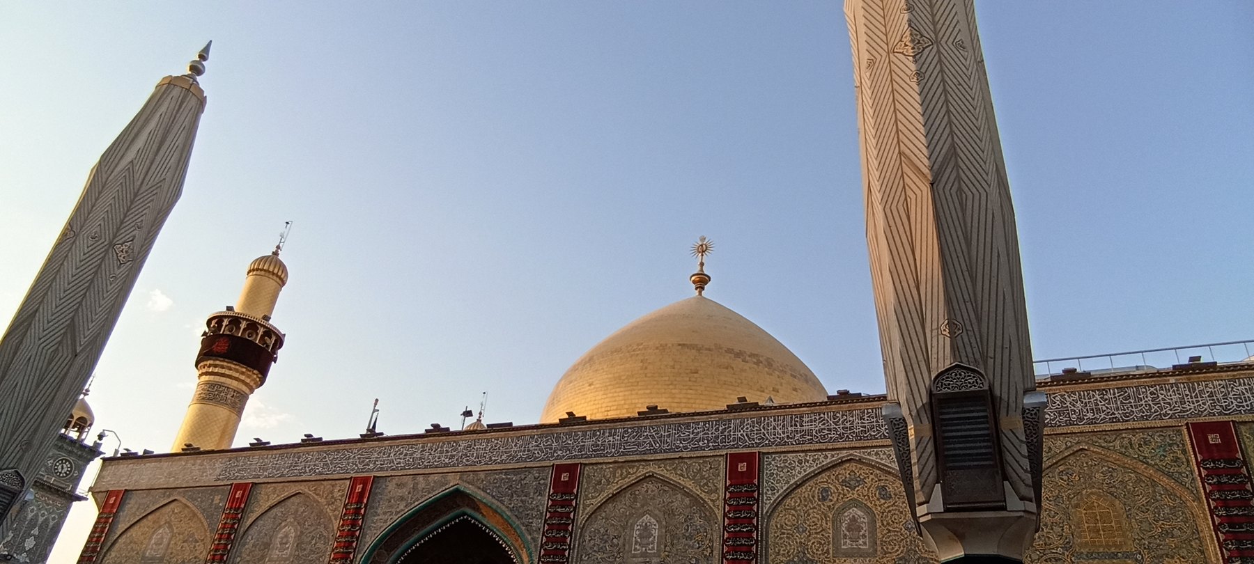 The gilded dome of the Imam Ali shrine in Najaf at dawn, framed between two tiled iwan pillars