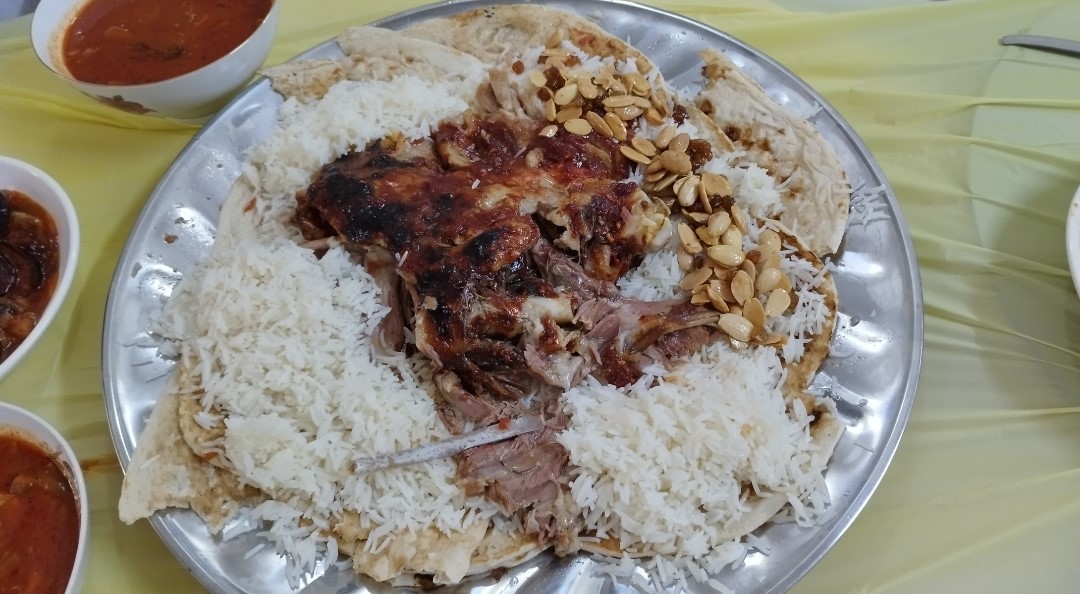 Iraqi quzi, slow-cooked lamb served over rice with almonds on a communal metal platter