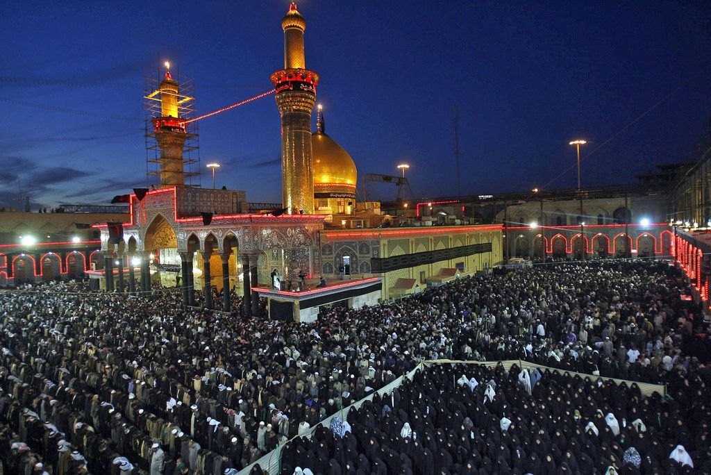 Thousands of worshippers at evening prayer in the courtyard of the Imam Hussein shrine in Karbala at blue hour