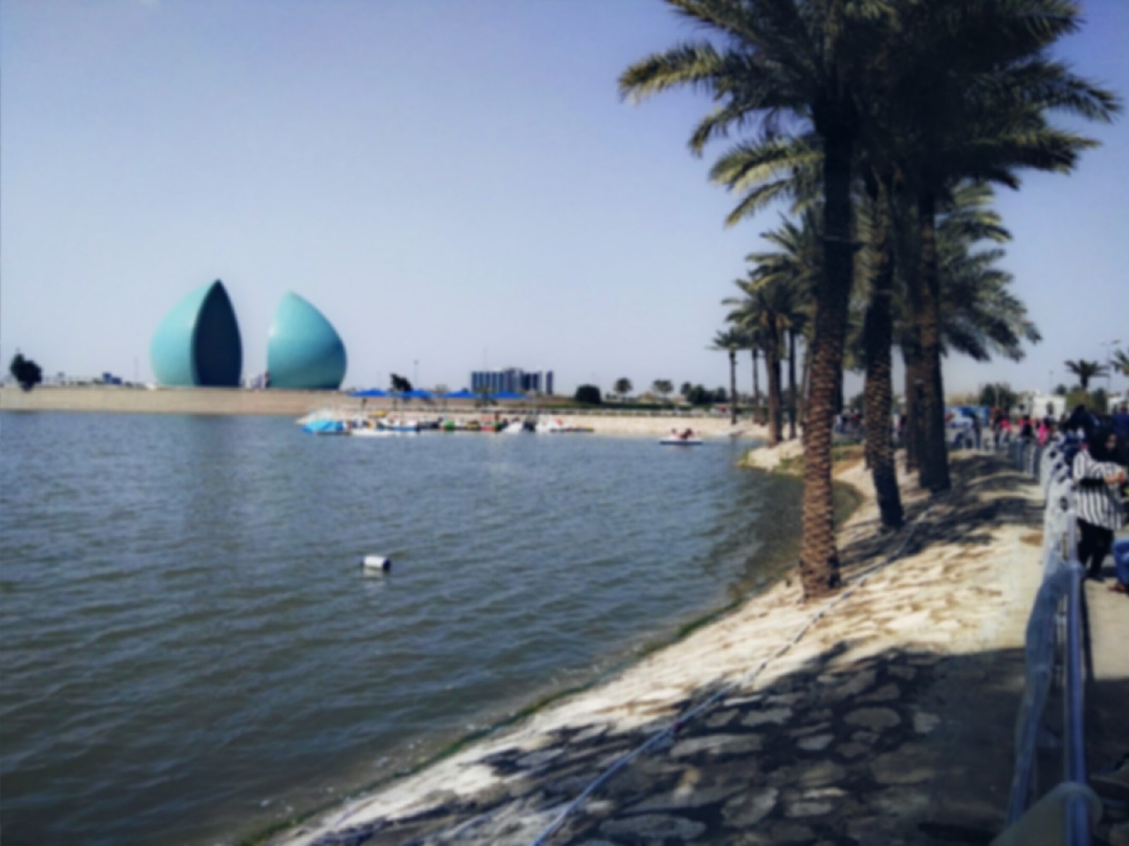 The Al-Shaheed Monument seen across its artificial lake, with pedal boats and families on the far shore