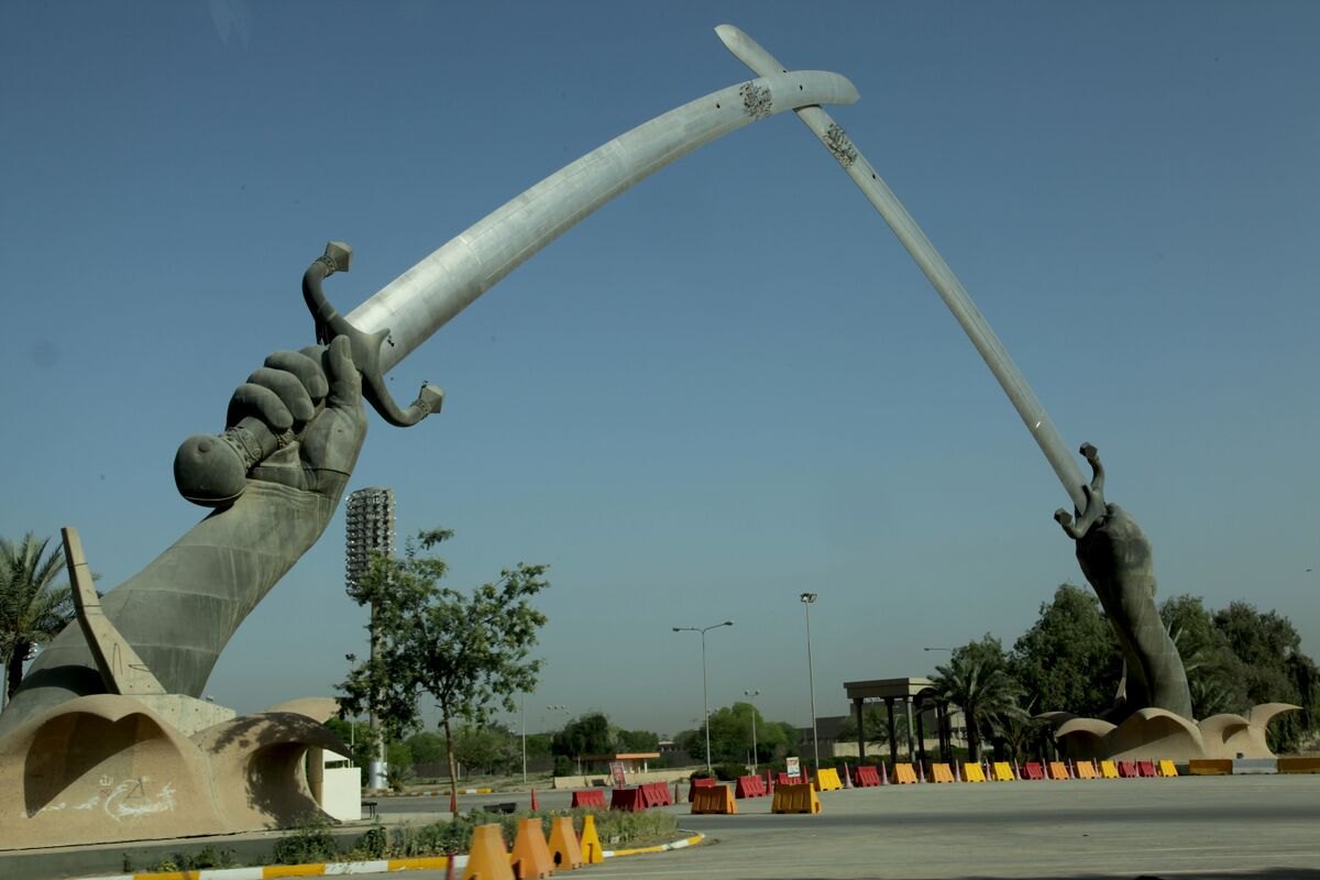 The Victory Arch, or Swords of Qadisiyah, in west Baghdad, with red and white road barriers across the parade ground in front of it