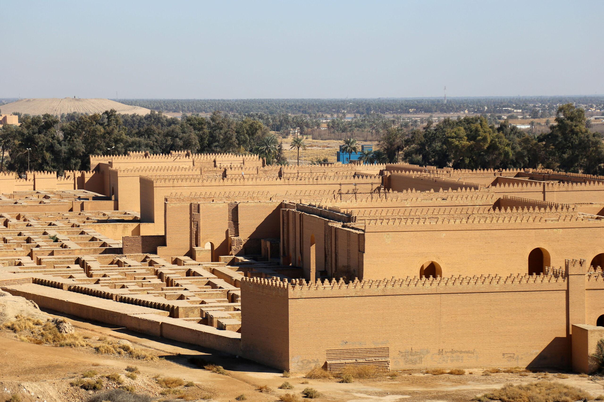 Reconstructed mud-brick walls of the Southern Palace at Babylon seen from above, with palm groves beyond