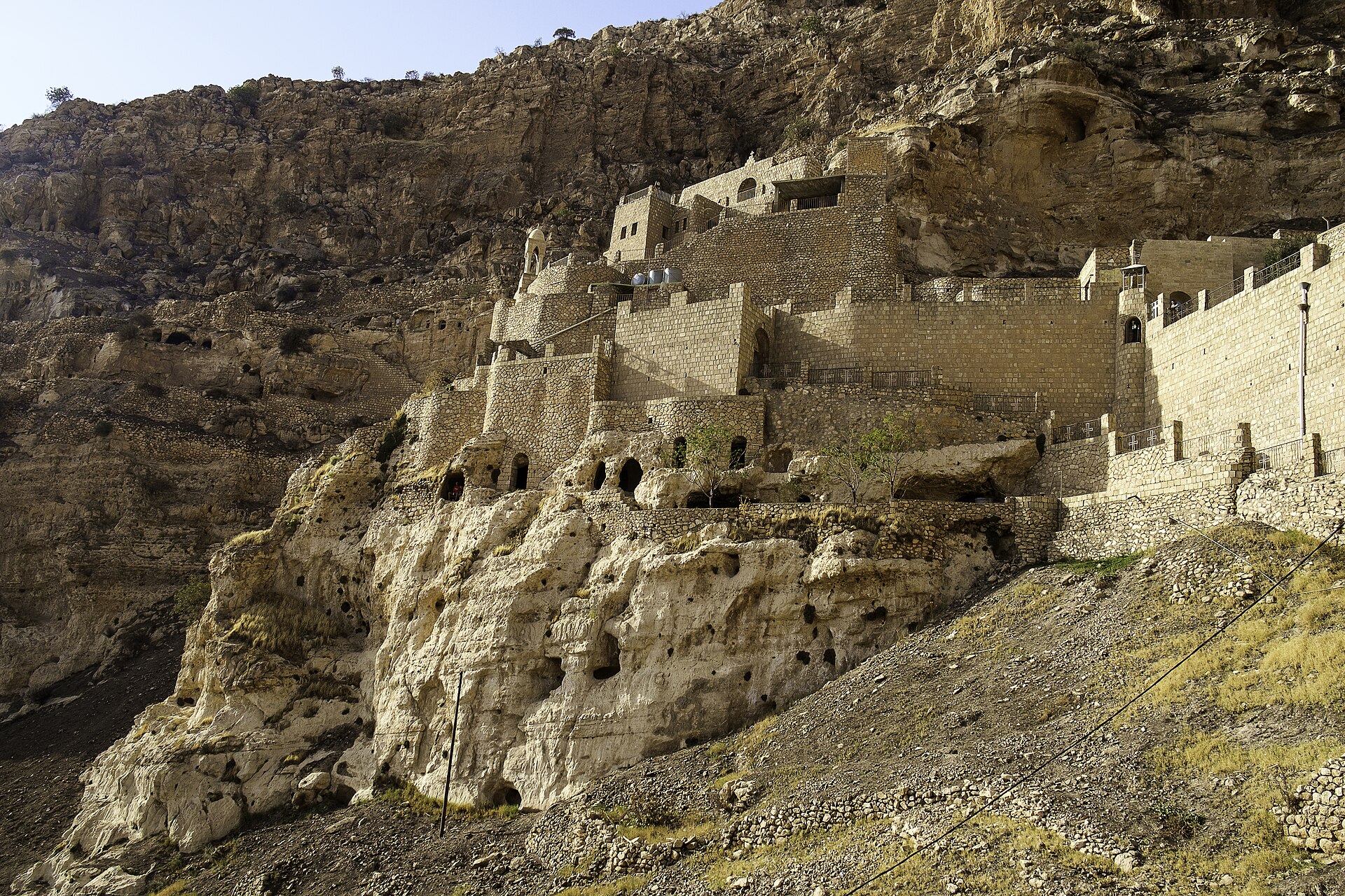 The Rabban Hormizd monastery built into a limestone cliff above Alqosh, with cave openings cut into the rock below it