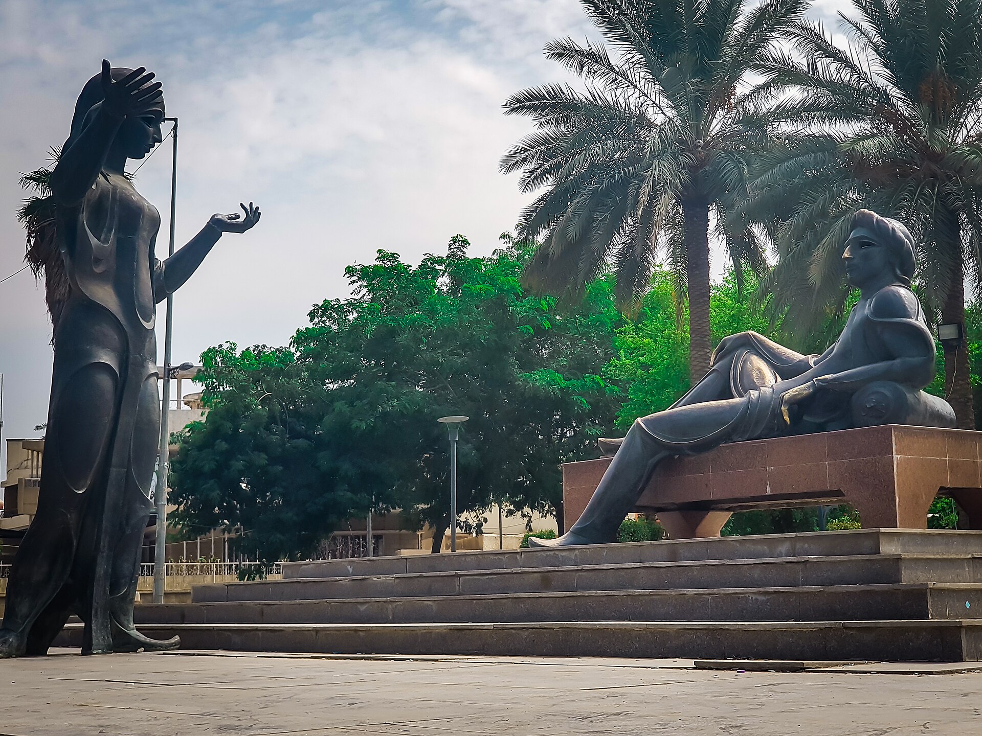 Bronze statues of Scheherazade standing and Shahryar reclining beside palm trees on Abu Nuwas Street, Baghdad