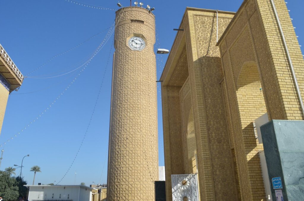 The brick clock tower and tall arched entrance of the Abu Hanifa Mosque in Adhamiya, Baghdad