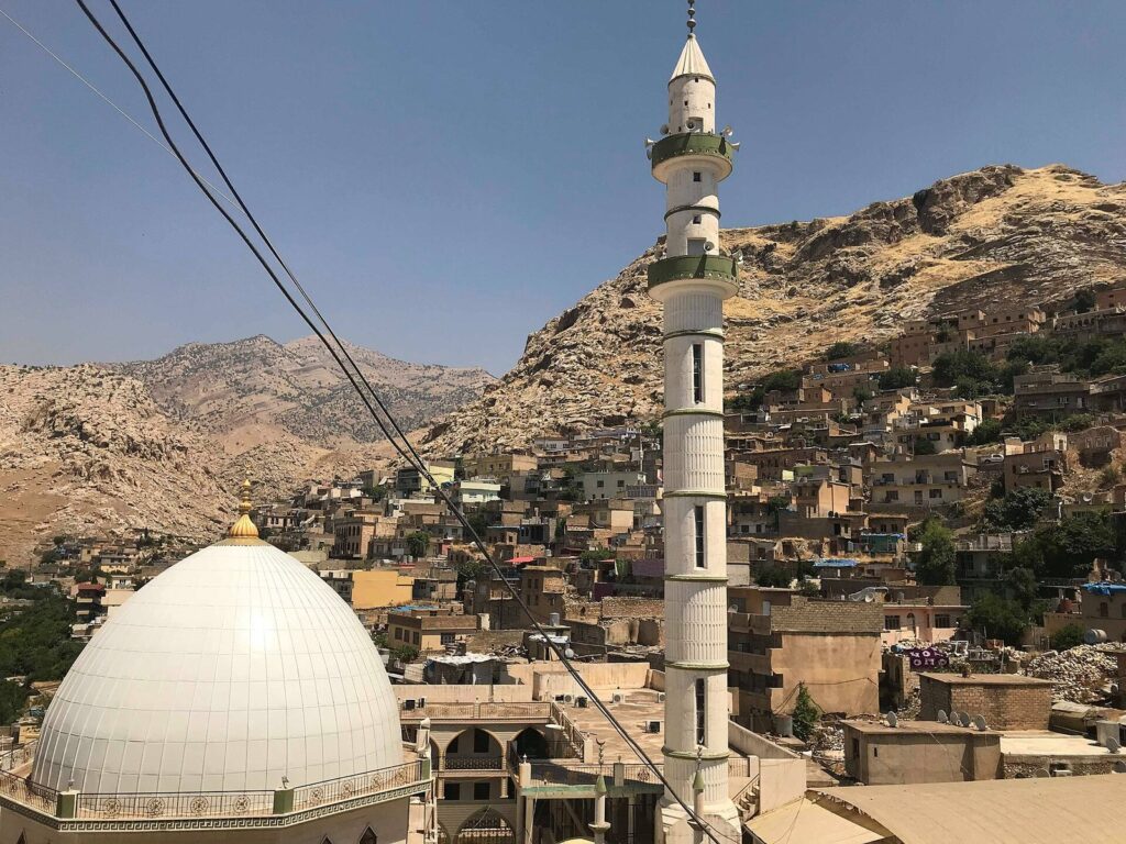 A white-domed mosque and minaret in Akre with the old town on the mountain behind