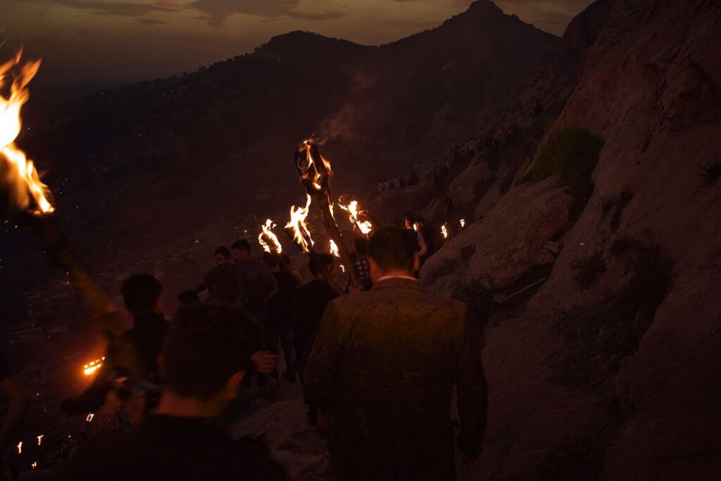 Akre Newroz torch-bearers climbing a rocky mountain path at dusk