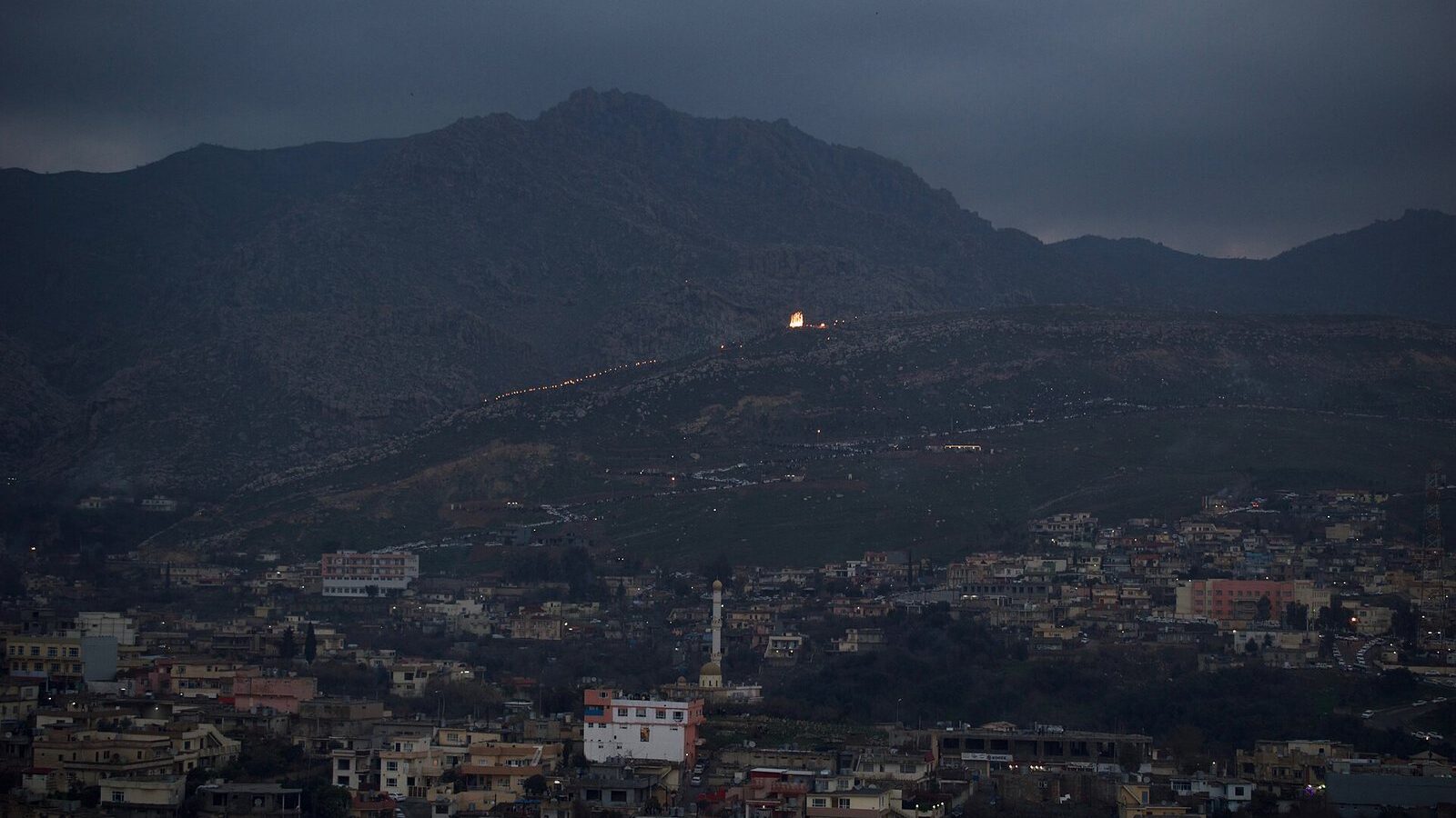 The town of Akre at dusk with a line of Newroz torches climbing the dark mountain above it
