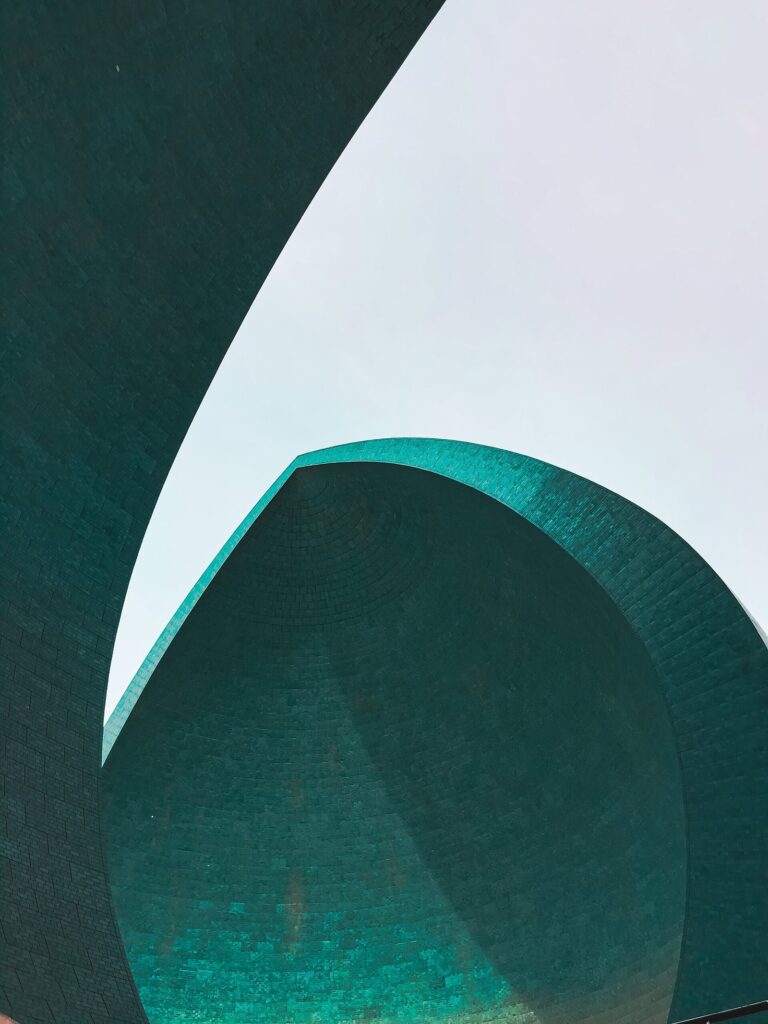Close view of one turquoise half-shell of the Al-Shaheed Monument in Baghdad against a pale sky