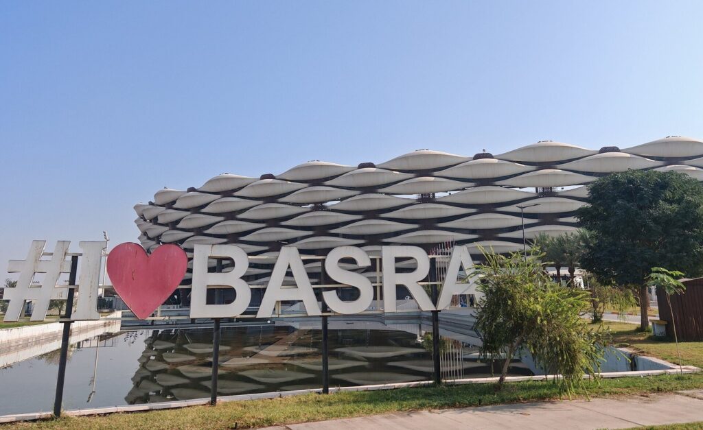 The Basra International Stadium with its palm-trunk columns behind a large I Love Basra sign