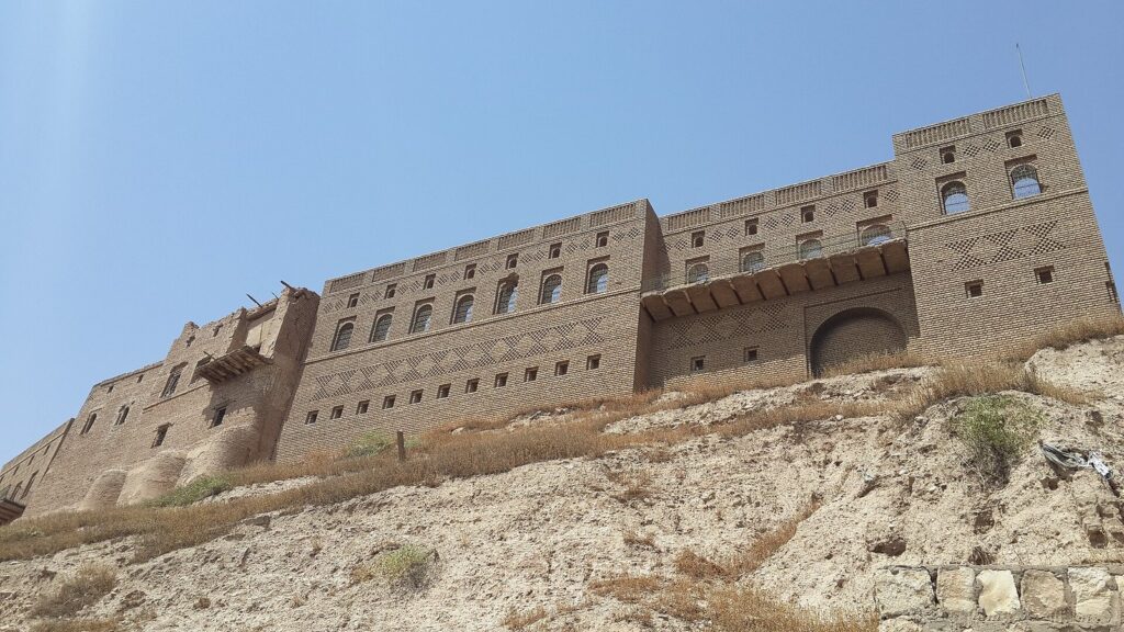 The restored brick facade of Erbil Citadel's outer houses rising above the grassy slope of the mound