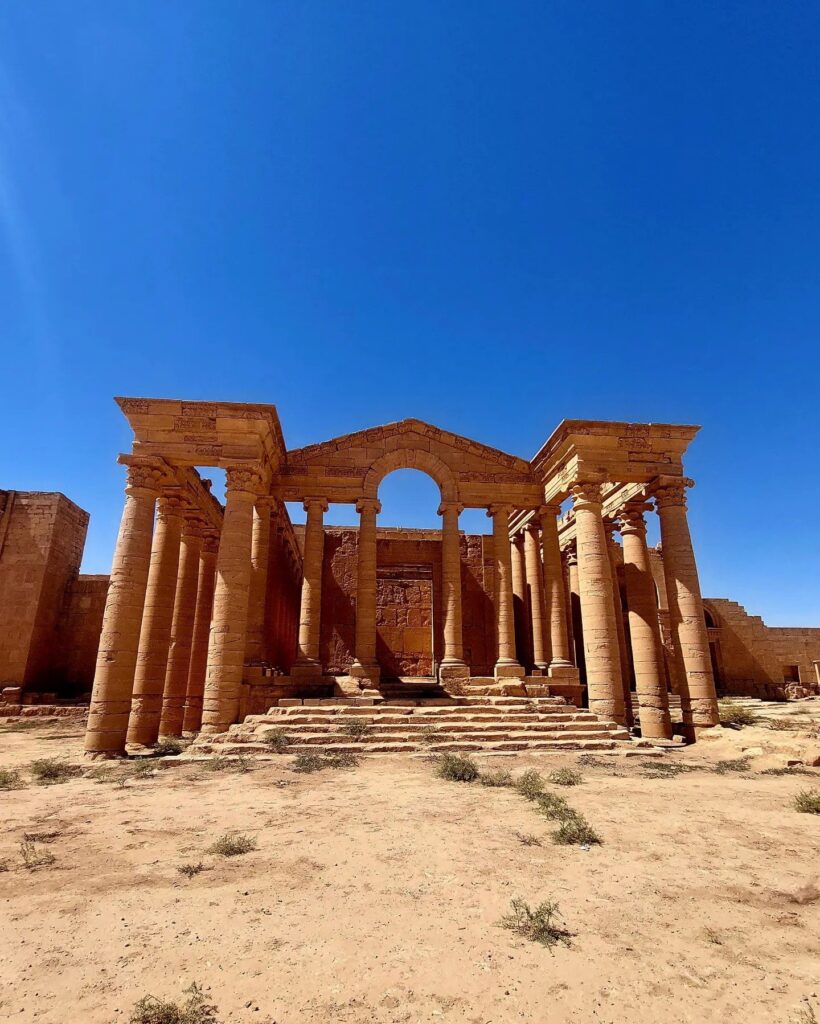 The columned façade of a temple at Hatra with a central arch, standing against a deep blue sky