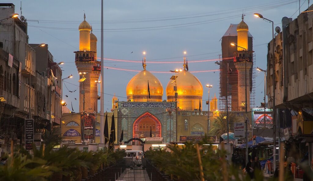 The twin golden domes and minarets of the Kadhimiya shrine in Baghdad lit at dusk at the end of a street
