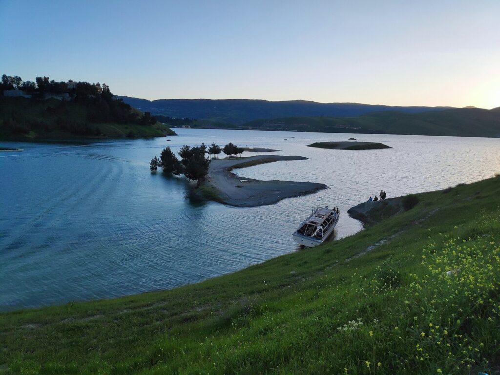 Lake Dukan in spring with green grass on the shore and a boat moored below, in the best time to visit Kurdistan