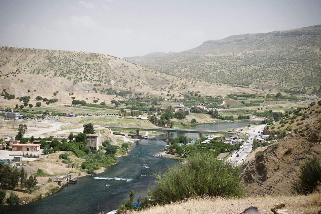 The Lesser Zab river winding through a green valley below Dukan Dam with the town on its banks
