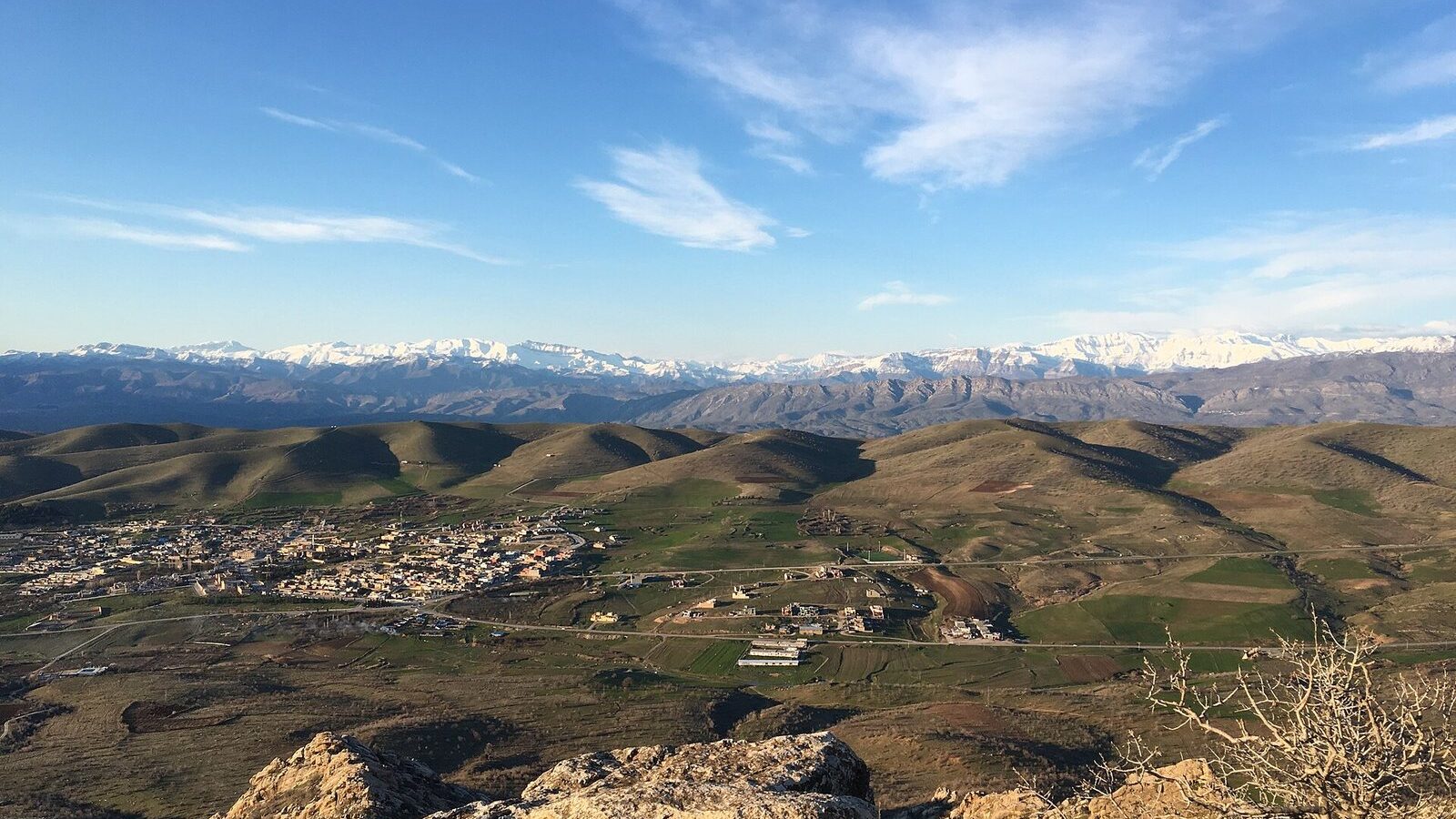The town of Mangesh among rolling foothills with snow-covered mountains on the horizon in the Kurdistan Region