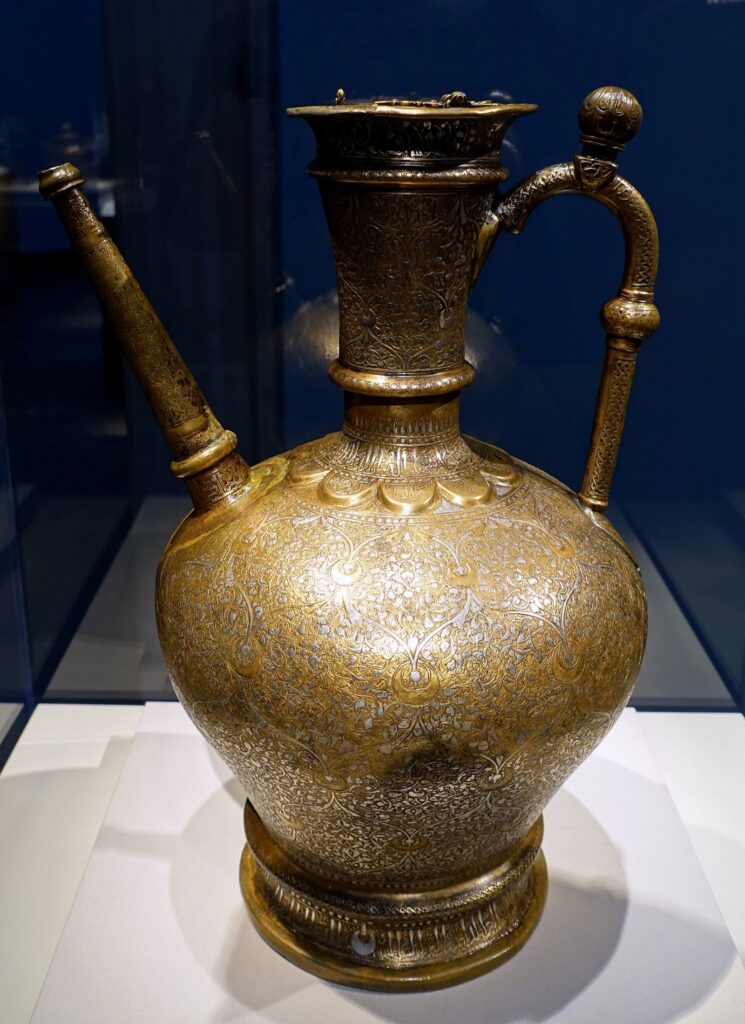 A brass ewer with silver inlay made in Mosul and dated Ramadan 629 AH, displayed in a museum case