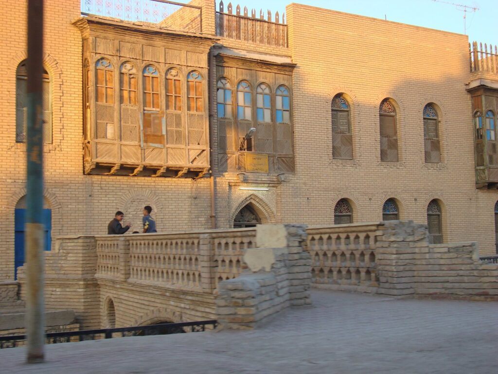 An old Basra merchant house with carved wooden shanasheel balconies above a canal-side terrace
