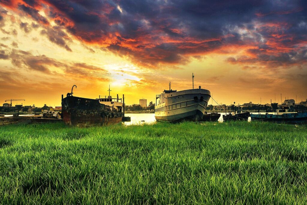 Old riverboats moored on the grassy bank of the Shatt al-Arab at Basra under an orange evening sky