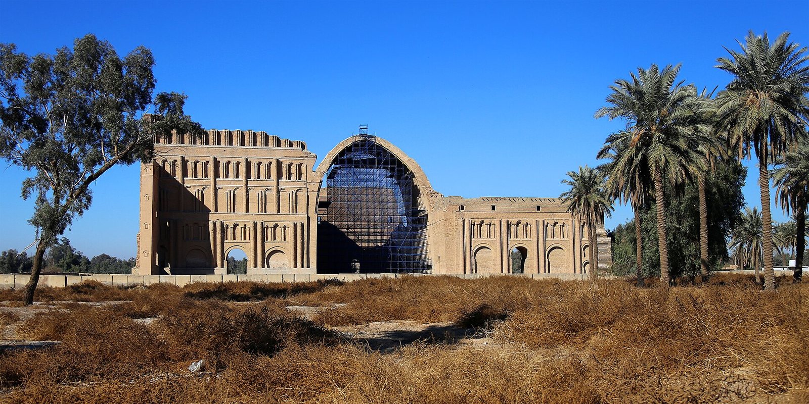 Taq Kasra, the great brick arch of Ctesiphon, with steel scaffolding inside the vault and palms around it